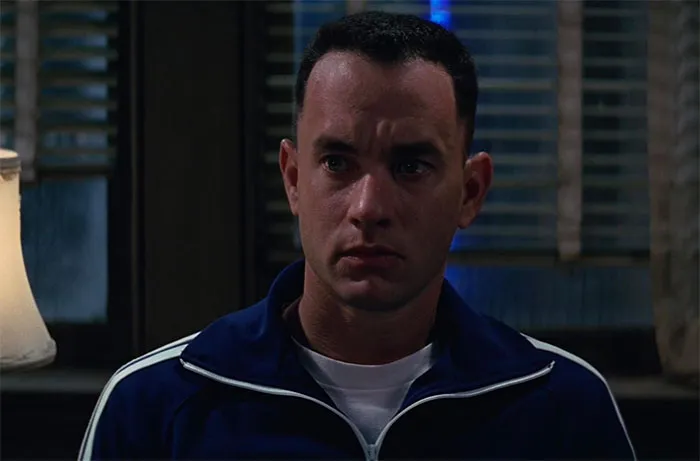Forrest Gump in a blue jogging suit, capturing a thoughtful moment related to iconic Forrest Gump quotes.