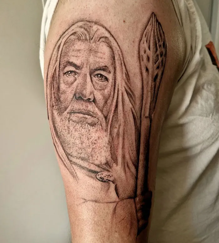 Lord of the Rings tattoo depicting a wizard holding a staff on an upper arm.