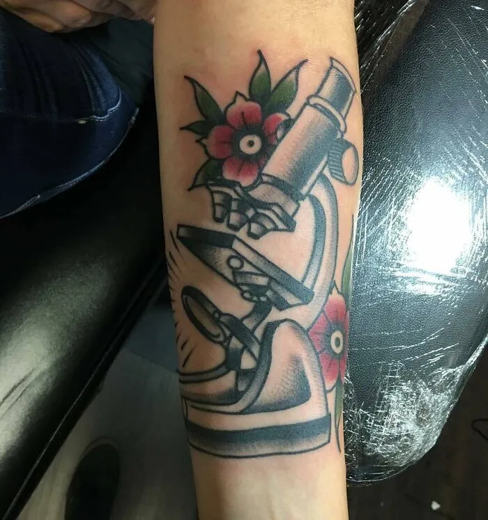 Microscope tattoo on forearm with colorful floral accents, ideal for science enthusiasts.