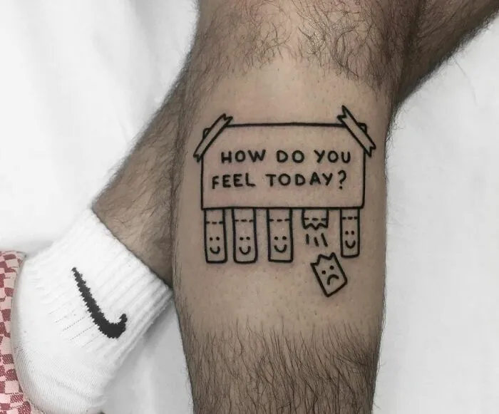 Tattoo of a sign with "How do you feel today?" and detachable paper face illustrating mental health on a leg.