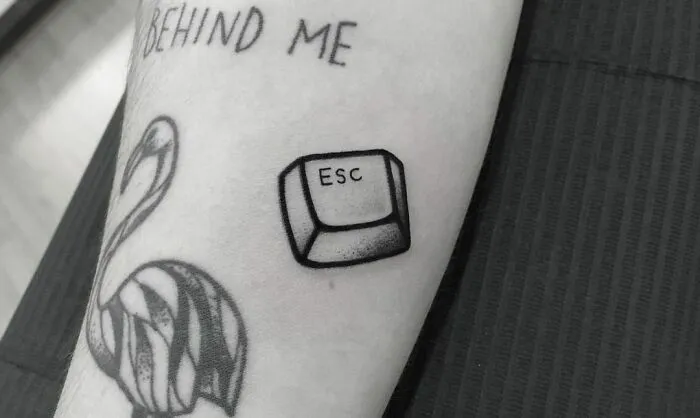 Mental health tattoos featuring an "ESC" key and a flamingo design on an arm.