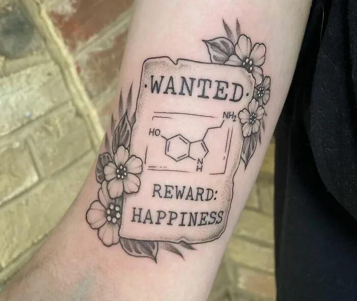 Mental health tattoo featuring a chemistry structure, text "Wanted: Reward: Happiness," surrounded by floral design.