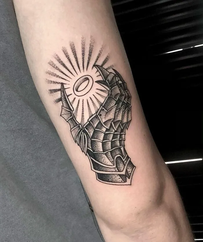 Arm tattoo of armored hand holding a ring emitting rays, inspired by Lord of the Rings.
