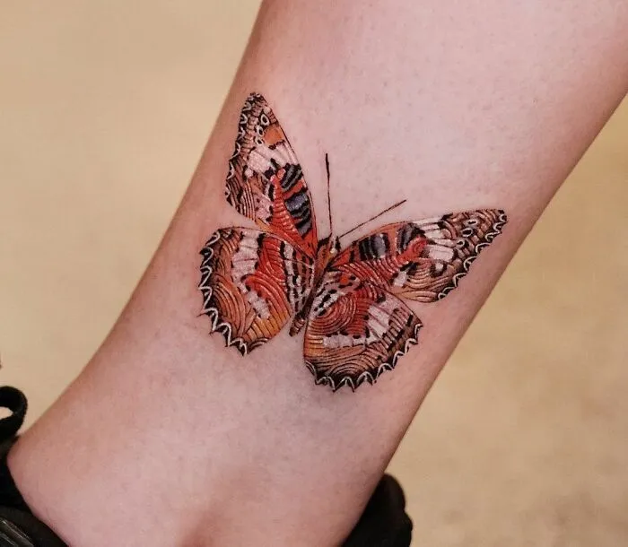Colorful butterfly tattoo on ankle, vibrant and realistic design.