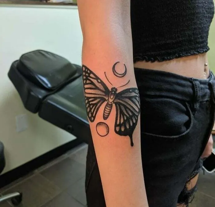 Butterfly tattoo on forearm with moon and circle designs, showcasing creative and colorful body art.