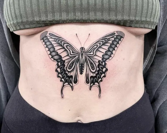 Black and gray butterfly tattoo on lower back, showcasing intricate and detailed wings.