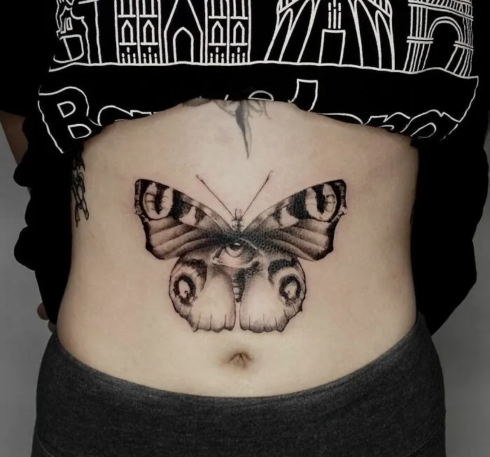 Butterfly tattoo on a person's abdomen, featuring intricate black and gray patterns and detailed shading.