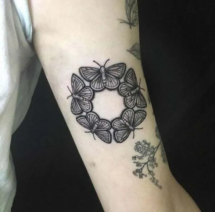 Black butterfly tattoo in circular design on forearm.