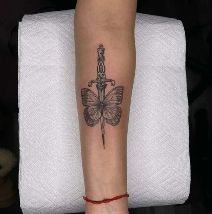 Butterfly tattoo with dagger design on forearm, showcasing intricate black ink details.
