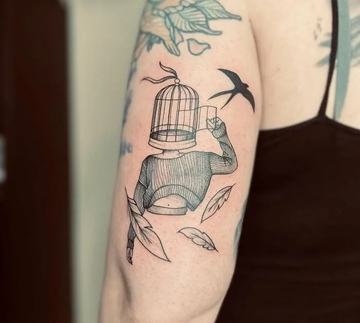 Tattoo of a woman with a birdcage head holding a glass, surrounded by flying feathers, symbolizing mental health freedom.