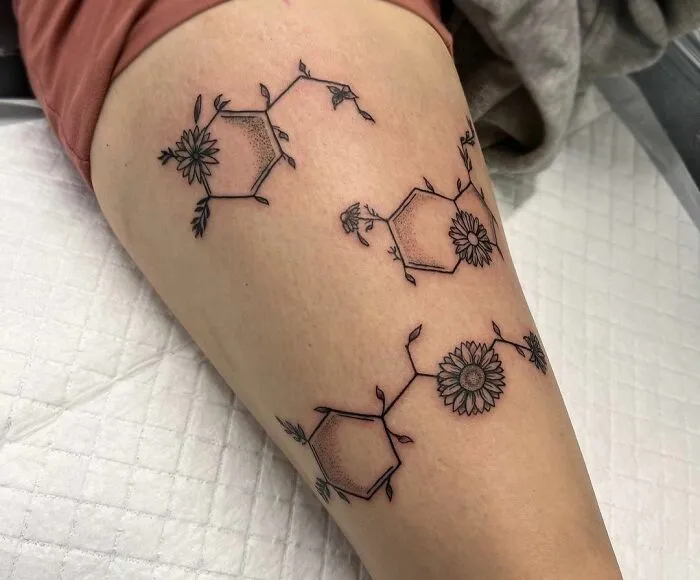 Tattoo of serotonin molecule with flowers on the thigh, symbolizing mental health and healing.