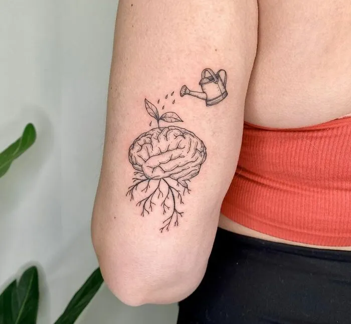 Mental health tattoo of a brain with roots and leaves being watered, symbolizing growth and healing.