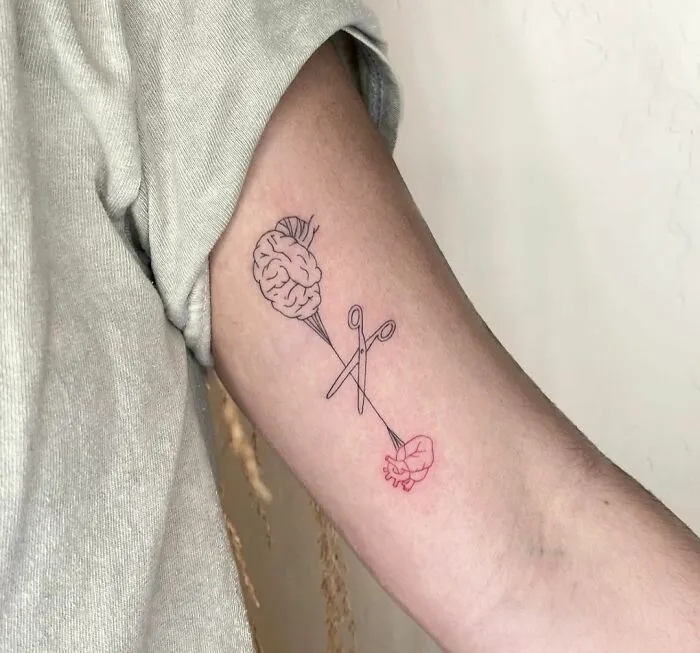 Tattoo of brain and heart connected by scissors, symbolizing mental health and healing.