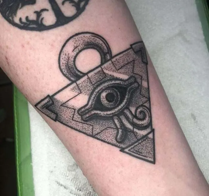 Anime tattoo featuring an artistic design resembling an eye symbol within a geometric shape on an arm.