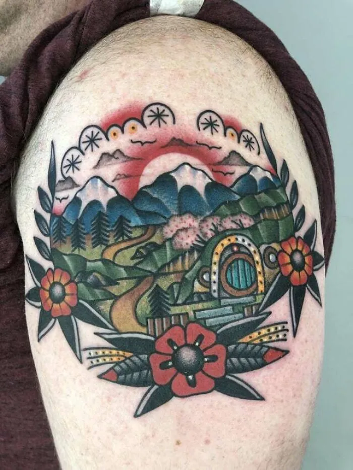 Colorful Lord of the Rings tattoo featuring a landscape with mountains, a winding path, and floral designs.