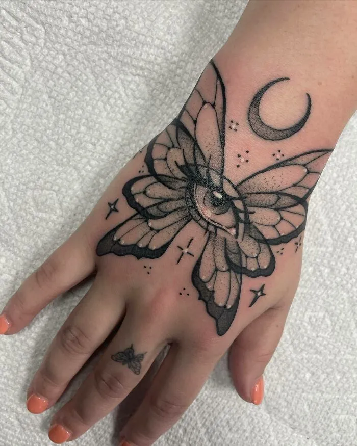 Butterfly tattoo with an eye and moon on hand, small butterfly on finger.
