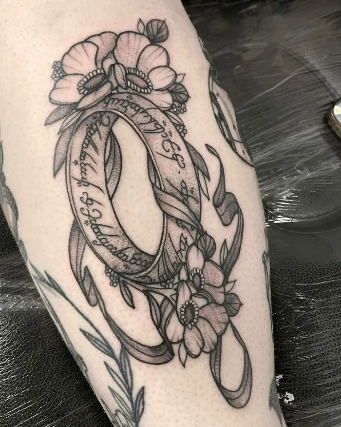 Lord of the Rings tattoo featuring a floral design and script on skin.
