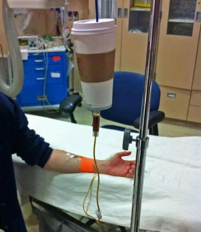 A coffee meme featuring an IV drip connected to a large coffee cup, humorously implying that the person is receiving coffee intravenously. The image playfully exaggerates the idea of needing coffee as a lifeline, capturing the essence of coffee addiction in a lighthearted and exaggerated manner.