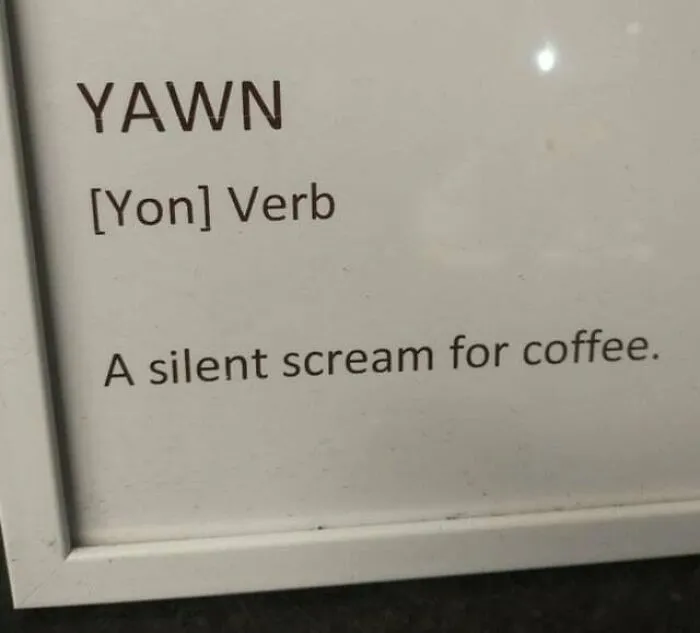 A coffee meme featuring a framed sign that humorously defines the word "Yawn" as "[Yon] Verb: A silent scream for coffee." The meme playfully suggests that yawning is a way of expressing the need for coffee, likening it to a cry for help in the form of caffeine.