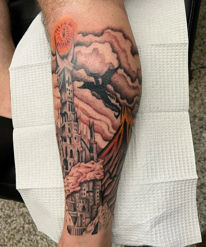 Lord of the Rings tattoo featuring a dark tower, fiery eye, and flying dragon on a leg.