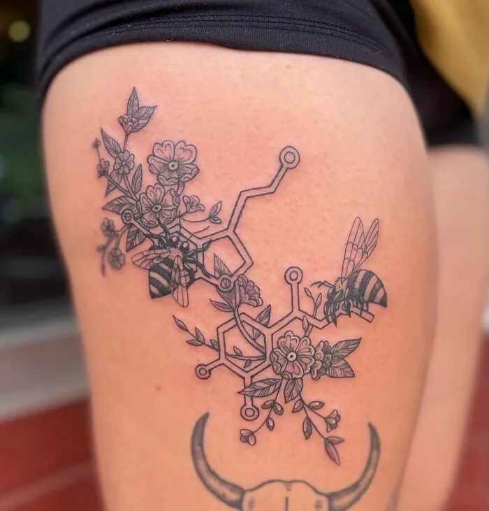 Science tattoo with floral and bee design on the thigh, featuring a chemical structure.