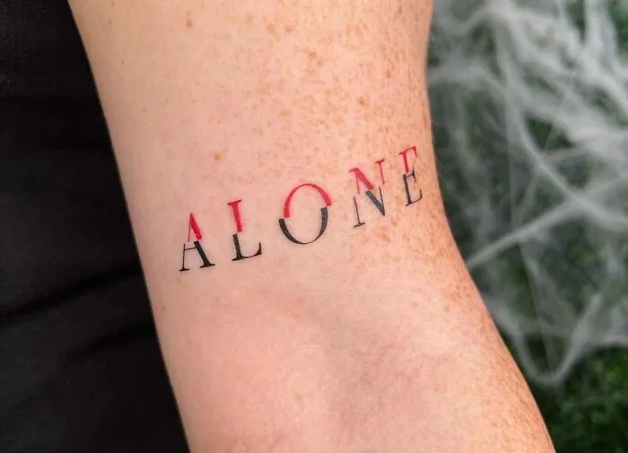 Tattoo of the word "alone" on an arm, symbolizing mental health and healing through bold black and red lettering.
