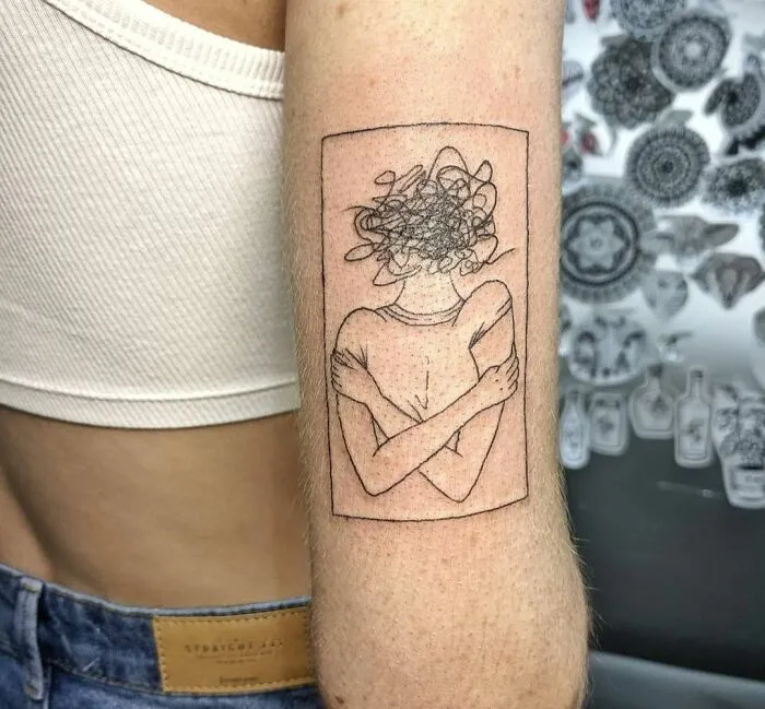 Minimalist tattoo of a person hugging themselves with a scribbled head, symbolizing mental health challenges and healing.