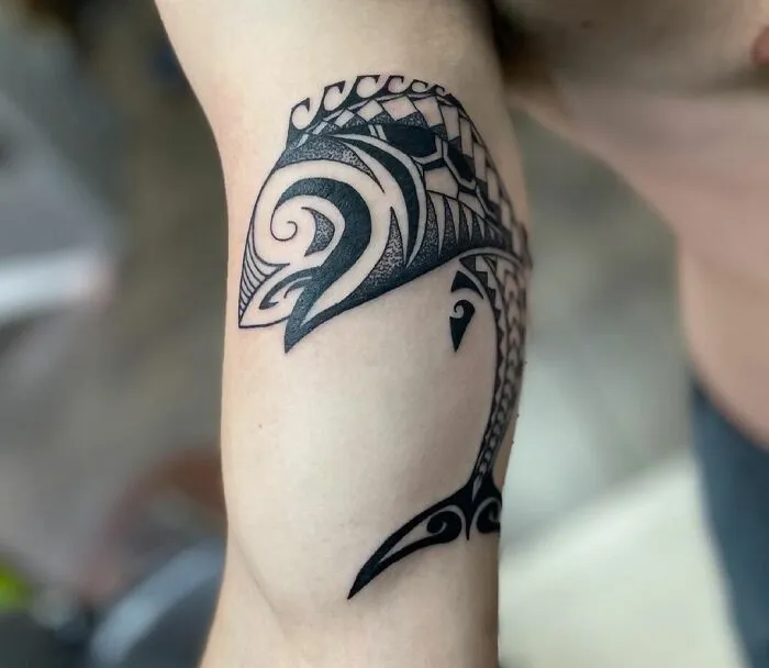 Intricate tribal tattoo of a stylized sea creature on an upper arm.