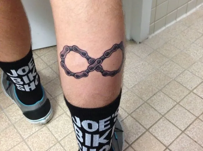 Infinity tattoo made of a bike chain on a person's leg, showcasing eternal creativity.