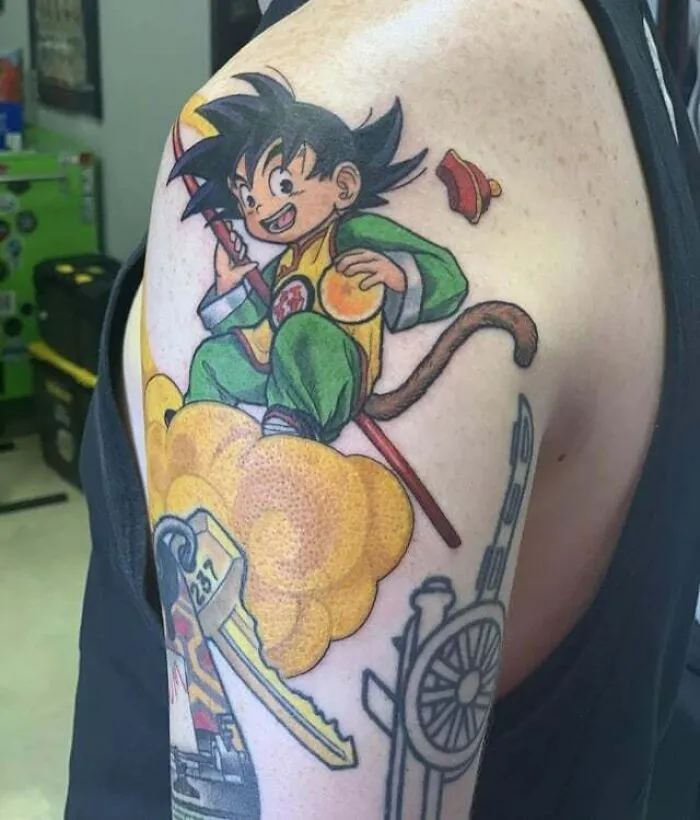 Anime tattoo featuring a cartoon character riding a yellow cloud on a person's upper arm.