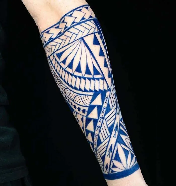 Forearm with intricate blue tribal tattoo design featuring geometric patterns.