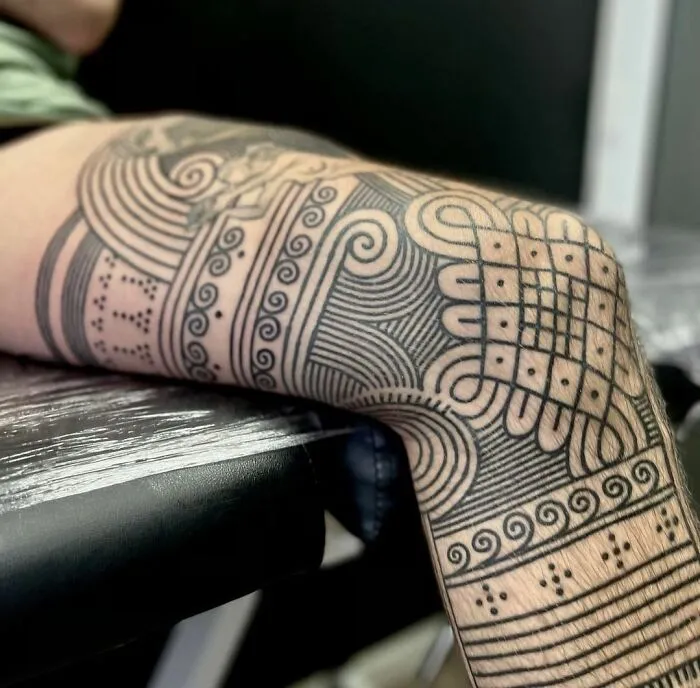 Close-up of a detailed tribal tattoo on a person's leg, showcasing intricate patterns and bold lines.