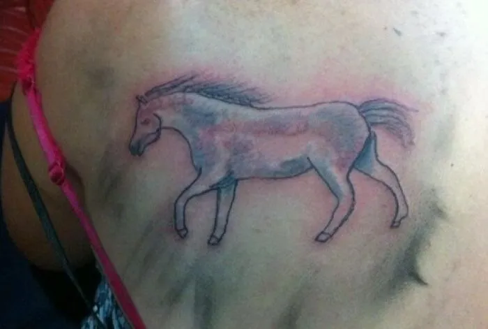 Poorly drawn horse tattoo on a person's back, showcasing a tattoo fail with faded colors and awkward anatomy.