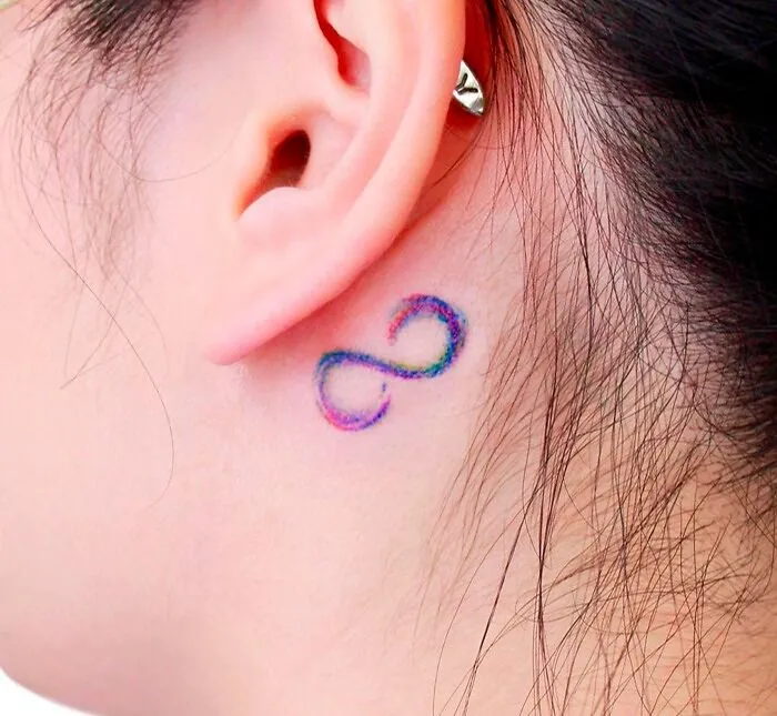 Colorful infinity tattoo behind the ear representing creativity and eternity.