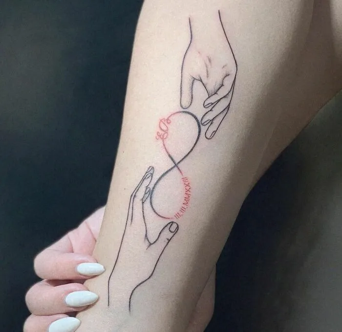 Infinity tattoo on an arm with two hands holding an infinity symbol, showcasing eternal creativity.