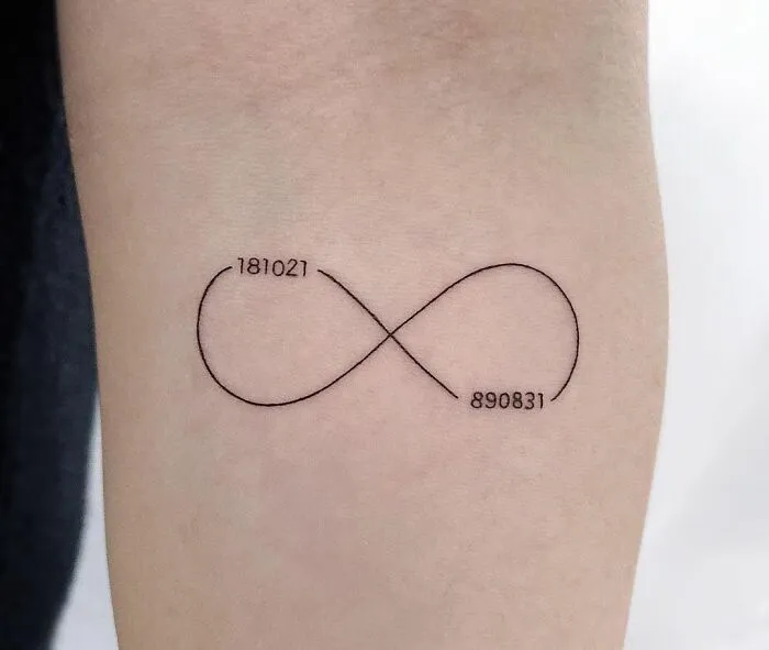 Infinity tattoo with numbers 181021 and 890831 on skin, symbolizing eternal creativity.