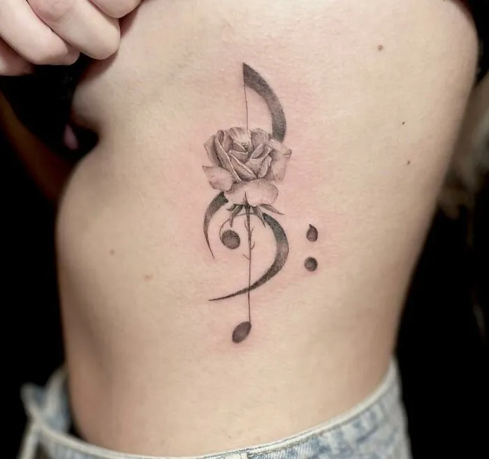 Tattoo of a rose integrated with a treble clef, symbolizing music and art on skin.