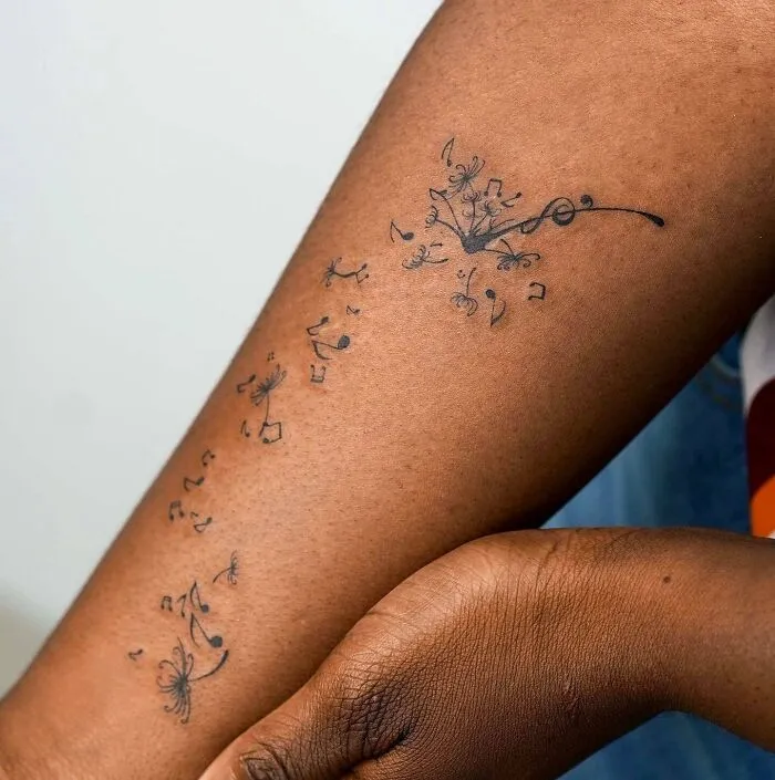 Arm with a delicate music tattoo featuring flowing notes and a floral design.