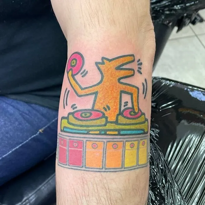 Colorful DJ scene music tattoo with a cartoon character spinning records on a turntable.