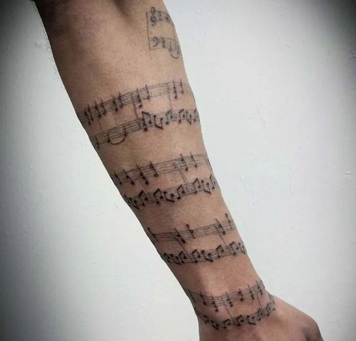Forearm adorned with intricate music tattoos featuring detailed sheet music notes.