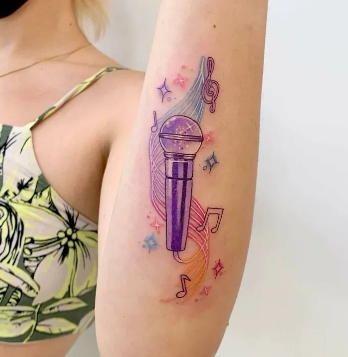 Colorful music tattoo featuring a purple microphone, musical notes, and swirls on a person's arm.