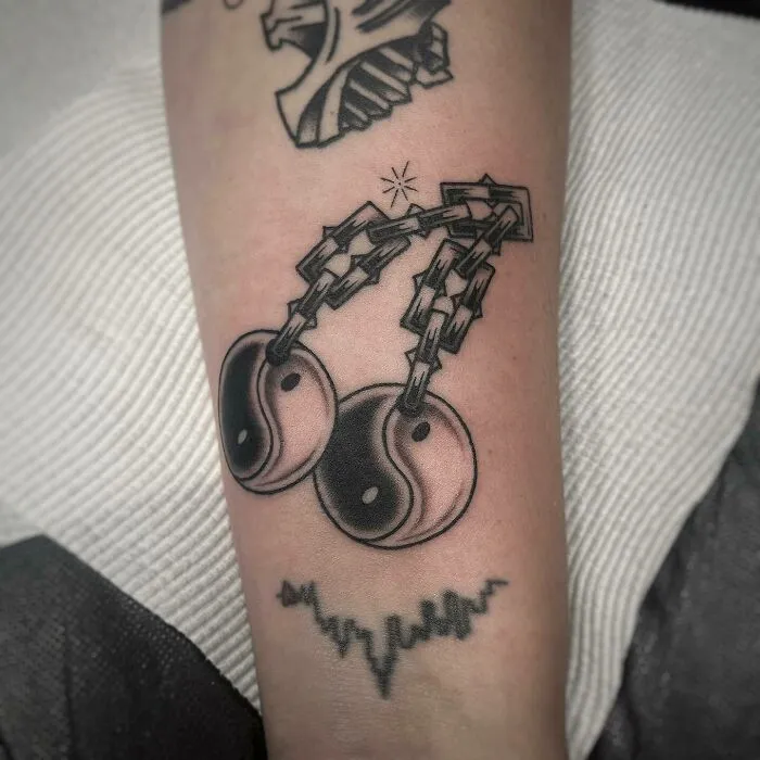 Tattoo of yin yang symbols connected by chains on an arm, symbolizing duality.