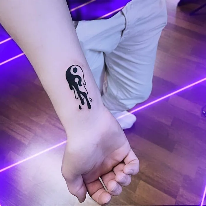 Melting yin yang tattoo on wrist, symbolizing life's duality.