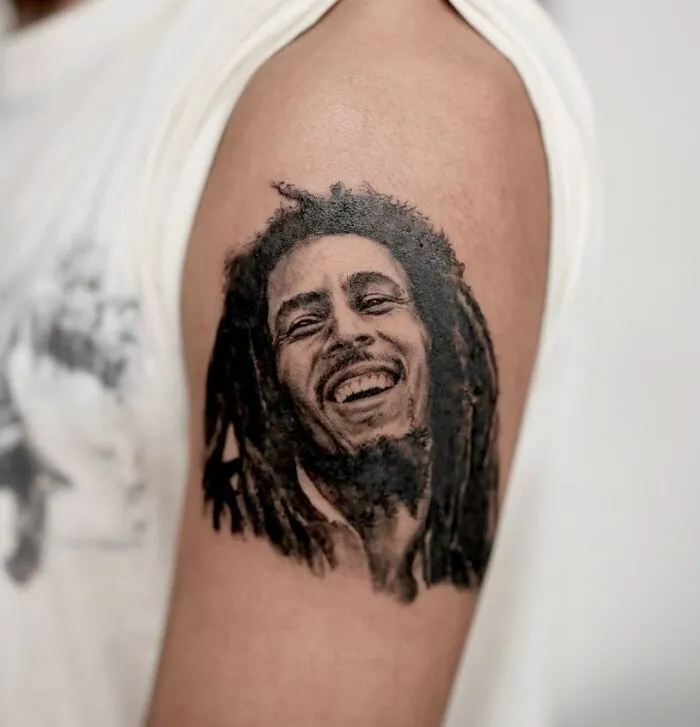 Portrait music tattoo on upper arm featuring a smiling musician icon.