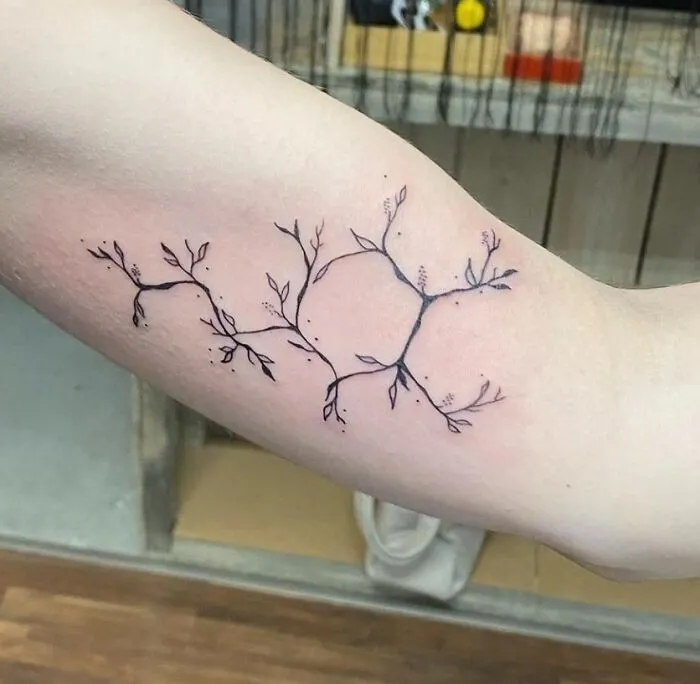 Minimal branch-like science tattoo on inner arm.