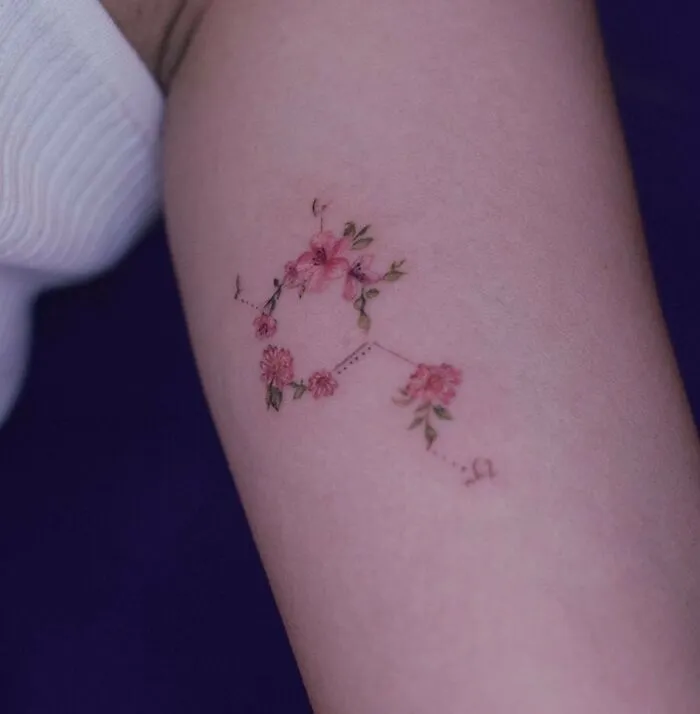 Floral constellation science tattoo on forearm, delicate pink flowers connected by dotted lines.