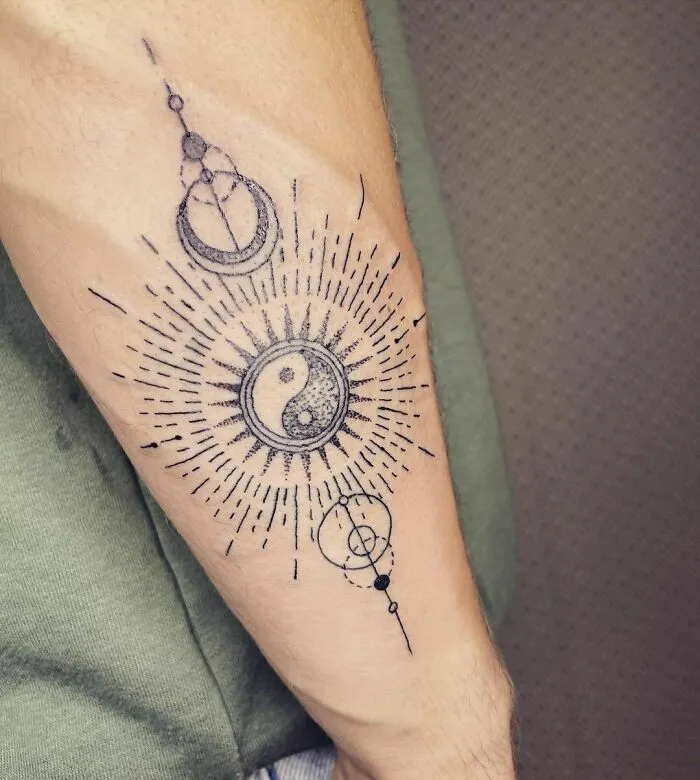 Yin Yang tattoo on forearm with intricate geometric patterns and sunburst design.