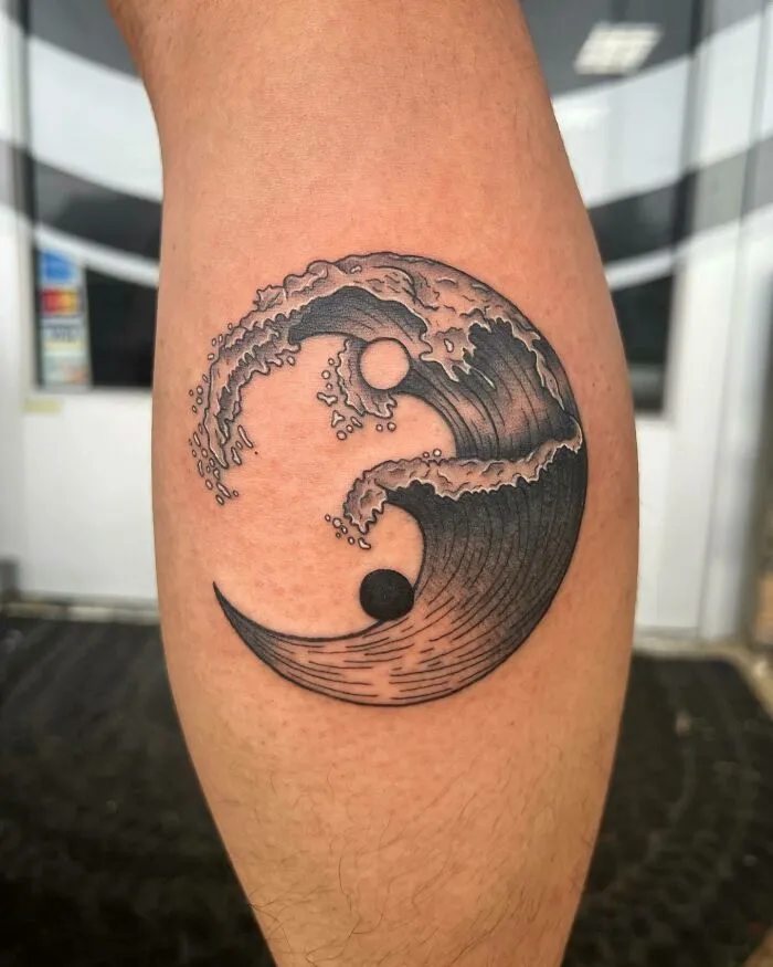 Yin Yang tattoo with water and wave design on an arm, symbolizing balance and duality.
