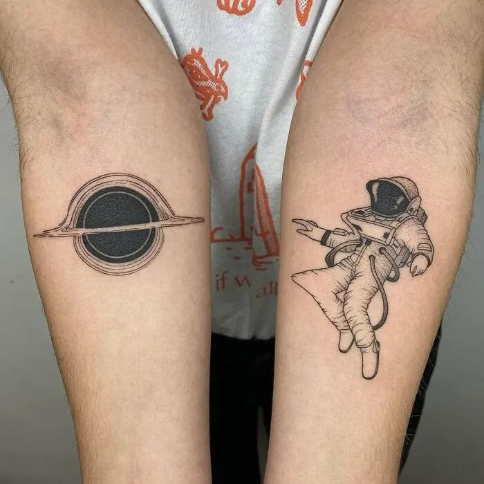 Astronaut and black hole tattoos on forearms, representing science and space exploration themes.
