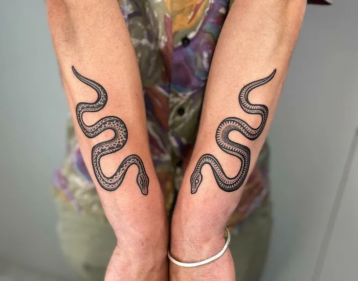 Snake tattoos on forearms, featuring intricate patterns and realistic detailing.